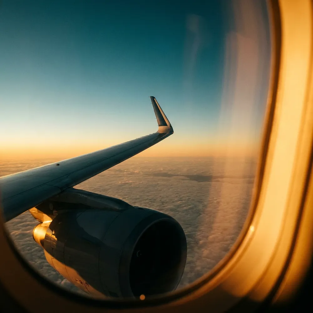 Aircraft wing over amber-lit clouds from a business class window